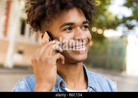 Nahaufnahme von lächelnden jungen afrikanischen Mann draußen, Gespräch am Handy Stockfoto