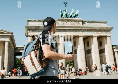 Eine Person hält eine Tasse mit Kaffee oder einem anderen Getränk beim Gehen oder Sightseeing in Berlin, Deutschland. Vor dem Brandenburger Tor und verschwommen, unbekannte Menschen. Stockfoto