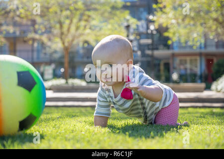 Lächelnd und aufgeregt Baby girl Kriechen nach Fußball im Freien Park Stockfoto