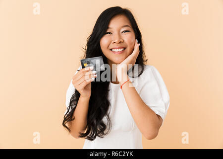 Portrait eines glücklichen jungen asiatischen Frau über beigen Hintergrund isoliert, holding Kunststoff Kreditkarte Stockfoto