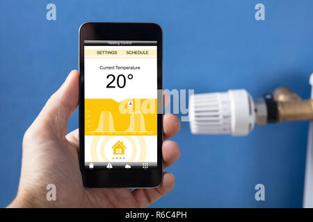 Person Festlegen der Hand Temperatur Thermostat mit Mobilephone Stockfoto