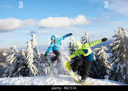 Zwei snowboarder Tricks bei Ski Resort. Reiter Freunde Durchführung springen mit ihren Snowboards in der Nähe von Wald auf backcountry Freeride Session in bunten modische Outfit. Copyspace Bereich. Stockfoto