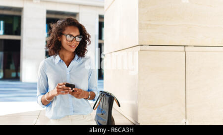 Lächelnde Frau mit Smartphone in den Händen. Unternehmer stehen draußen und weg schauen. Stockfoto