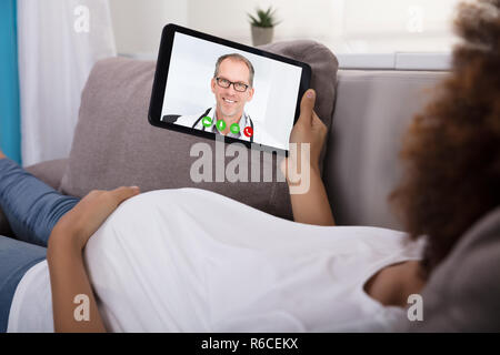 Schwangere Frau für Videokonferenzen mit Arzt auf Tablet Stockfoto