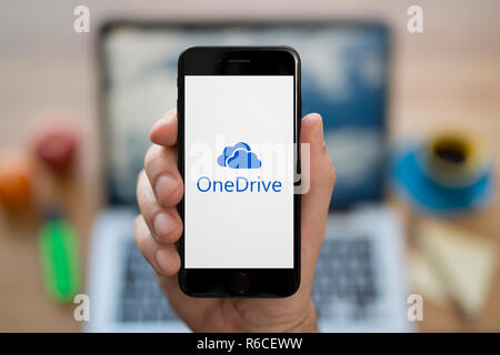 Ein Mann schaut auf seinem iPhone die zeigt den Microsoft OneDrive logo, während saß an seinem Computer Schreibtisch (nur redaktionelle Nutzung). Stockfoto