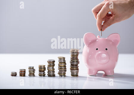 Person einfügen Münze in das Sparschwein Stockfoto