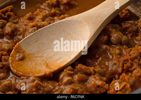 Kichererbsen Suppe mit Kartoffeln Zwiebeln in Tomatensauce kochen in einer Pfanne mit einem Holz Küche Löffel. Stockfoto