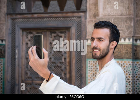 Junge muslimische Mann in traditioneller Kleidung lächelnd und unter selfie mit Handy Stockfoto