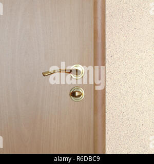 Part of new wooden door with yellow metal handle with lock in closed position indoor inside room wall covered with beige stucco vertical view close up Stockfoto