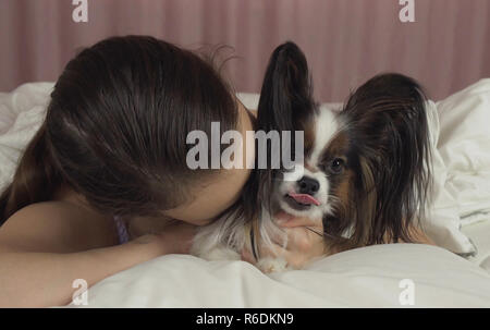 Gerne jugendlich Mädchen küsse und spielt mit Hund Papillon im Bett Stockfoto