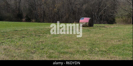 Amerikanische Flagge auf dem Ballen Heu mit Hand vor Pflug Stockfoto