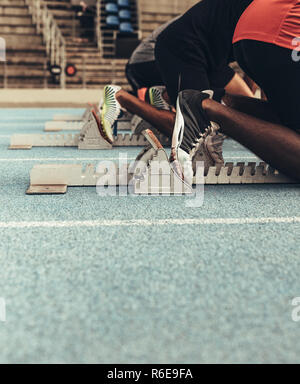 Sprinter auf ihre Markierung bereit auf einem alle Wetter Laufstrecke zu sprinten. Läufer mit einem startblock ihren Lauf auf der Rennstrecke zu starten. Stockfoto