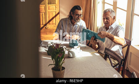 Zwei pensionierte Männer am Tisch sitzen und stricken zu Hause. Ältere Freunde machen wolle tragen mit Nadeln und Wolle Garn. Stockfoto