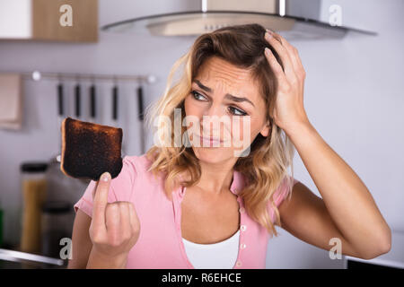 Frustrierte junge Frau mit Toast gebrannt Stockfoto