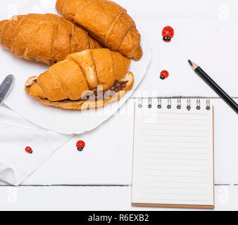 Drei gebackene Croissants mit Schokolade und eine Papier notepad Stockfoto