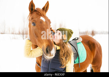 Weibliche Reiter und Pferd im Freien. Porträt einer schönen jungen Frau mit ihrem Hengst, im Freien im Winter. Mädchen umarmen und streicheln des Tieres Stockfoto