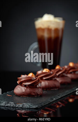 Dessert Schokolade mit Haselnuss und Kaffee mit Sahne auf einem schwarzen reflektierenden Hintergrund. Stockfoto