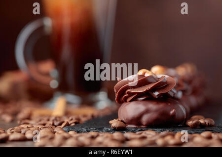Dessert Schokolade mit Haselnuss und Kaffee mit Sahne auf einem Holztisch. Kaffeebohnen und Zimtstangen liegen auf dem Tisch verstreut. Stockfoto
