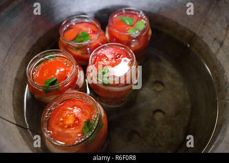 Canning frische Tomaten mit Zwiebeln in Gelee Marinade. Erhaltung und Kochen. Gläser in Wasser Bakterien zu töten. Abdichten. Basilikum, parsl Stockfoto