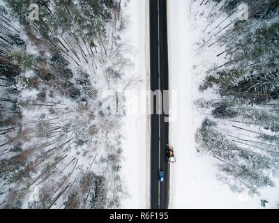 Winter Forest und Asphalt. Blick von oben. Das Foto wurde mit einer Drohne getroffen. Kiefer und Wald mit einem schwarzen Straße im Schnee Fichte. Stockfoto