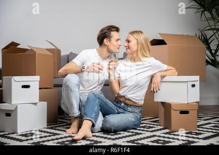 Foto des jungen Paares mit Champagner Gläser sitzen unter Kartons Stockfoto