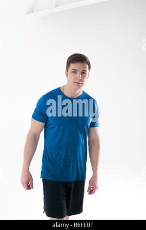 Junge muskulöse schönen athletischen Mann in Blau Sport Shirt, Shorts und Turnschuhen stehen auf weißen Hintergrund im Studio gekleidet Stockfoto