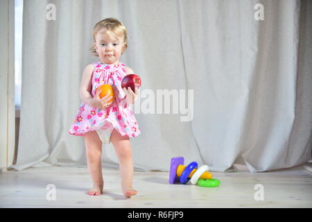 Hübsches kleines Mädchen in ein rosa Kleid mit roten Apfel und Orange in der Hand auf einem hellen Hintergrund Stockfoto