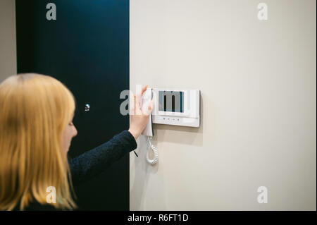 blonde Frau hängt den Hörer nach der Beantwortung der Sprechanlage rufen Sie in ihrer Wohnung Stockfoto