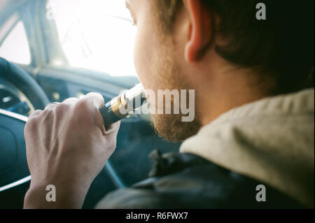 Junge vaper Mann mit Bart vaping mechanische Mod. Kerl eine elektronische Zigarette raucht, die durch Blasen einer Rauch, Dampf. Die RDA-Mundstück mit den Lippen auf bunten Hintergrund hinter dem Lenkrad sitzen Stockfoto