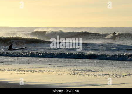 Ein Surfer erhält auf seine Füße auf einen frühen Welle mit einem Freund über ihn in den Untiefen melden Sie Stockfoto