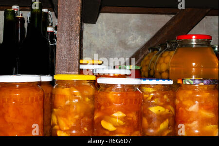 Apple, Cherry Plum in Gläsern und hausgemachten Wein in Flaschen im Keller. In der Nähe von Beständen gehalten für den Winter. Stockfoto