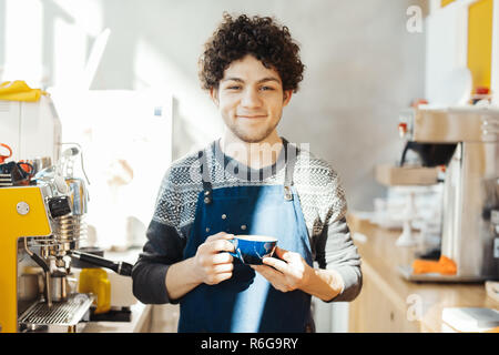 Barista und lächelnd Kaffeetasse in der Nähe der Theke in hellen, modernen Cafe. Stockfoto