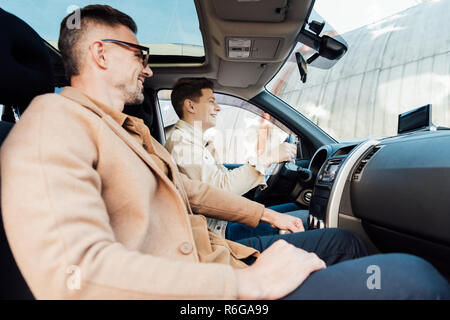 Seitenansicht der lächelnden schönen Vater Lehre jugendlich Sohn Auto Stockfoto