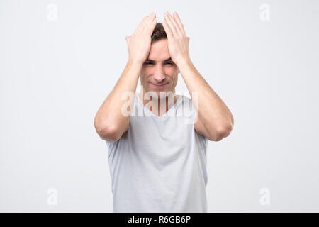 Verärgert unglücklichen jungen italienischen Mann den Kopf mit den Händen zusammendrücken, leiden unter Kopfschmerzen. Stockfoto