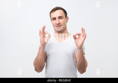 Ein hübscher junger italienischer Mann im grauen T-Shirt, das OK-Zeichen Stockfoto
