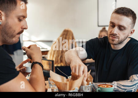 Zwei Freunde essen Burger und Pommes, Kaffee trinken im Cafe. Stockfoto