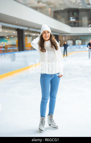 Lächelnde junge attraktive Frau in Form gestrickter Pullover Schlittschuhlaufen auf der Eisbahn allein Stockfoto