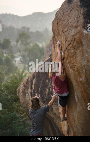 Ein männlicher Kletterer Praktiken, seine Fähigkeiten, Grip und Stärke Klettern ein Boulder mit einem Freund unter ihm Spotting für Sicherheit. Stockfoto