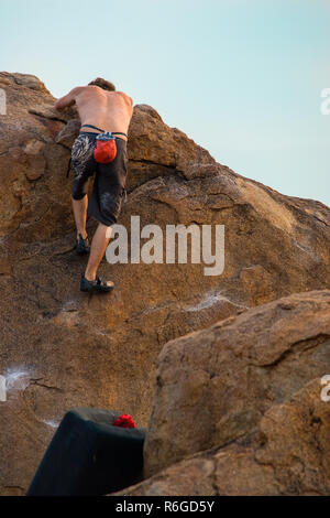 Ein männlicher Kletterer Praktiken, seine Fähigkeiten, Grip und Stärke Klettern ein Boulder mit einem Crash mat unter ihm für die Sicherheit. Stockfoto