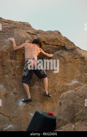 Ein männlicher Kletterer Praktiken, seine Fähigkeiten, Grip und Stärke Klettern ein Boulder mit einem Crash mat unter ihm für die Sicherheit. Stockfoto