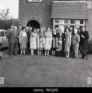 1960, historische, eine Familie außerhalb eines suburban Doppelhaushälfte für eine Gruppe Bild goldenen Hochzeit ein Paar zu feiern, England, UK zu stellen, sammeln. Eine goldene Hochzeit feiert 50 Jahre Eheleben, eine Vollendung von großer Liebe und Engagement. Stockfoto