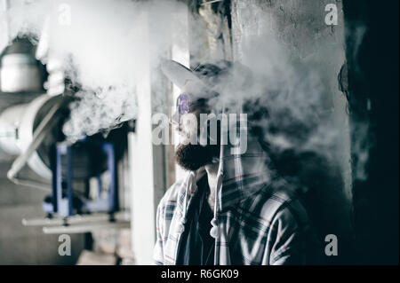 Junger Mann mit Bart in hell karierten jacke mit Kapuze in einem Gap raucht eine elektronische Zigarette in vape Bar Stockfoto