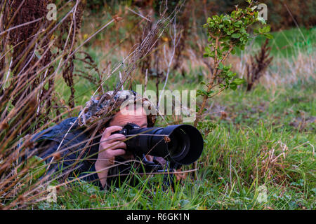 Naturfotograf versteckt im Gras, Büsche ohne sichtbares Gesicht. Stockfoto