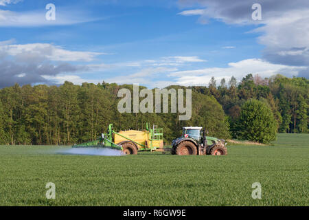 Bauer im Traktor spritzen Insektizide Herbizide //Pestizide über auf dem Feld mit der gezogenen Feldspritze im Frühjahr Stockfoto