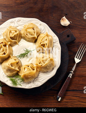 Asiatische gedünstete Teigtaschen Manti mit Dill und Knoblauch auf Holz- Hintergrund. Stockfoto