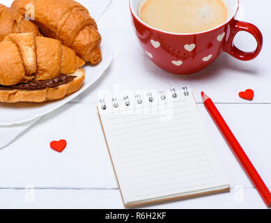 Leeren Notizbuch aus Papier, rot Tasse mit Kaffee und Croissants mit Schokolade Stockfoto