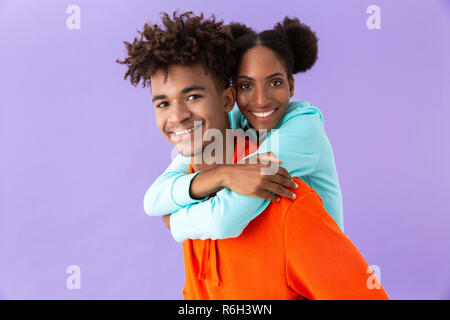 Foto der jungen afrikanischen amerikanischen Bruder huckepack Sein lächelndes Schwester über violette Hintergrund isoliert Stockfoto