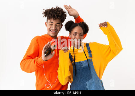 Foto von jungen afrikanischen amerikanischen Paar in bunten Kleidern tanzen, während Sie Musik hören mit Kopfhörern auf weißem Hintergrund Stockfoto