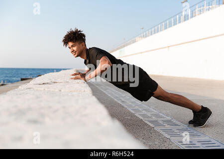 Bild der hübschen jungen Kerl Sportler machen Übungen im Freien am Strand. Stockfoto
