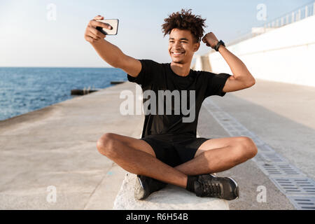 Glückliche junge afrikanische Sportler am Strand unter einem selfie, flexing Biceps Stockfoto
